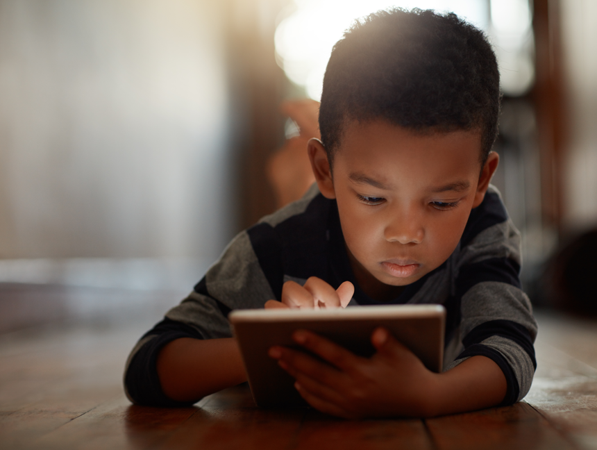 Young boy laying on floor while using a tablet