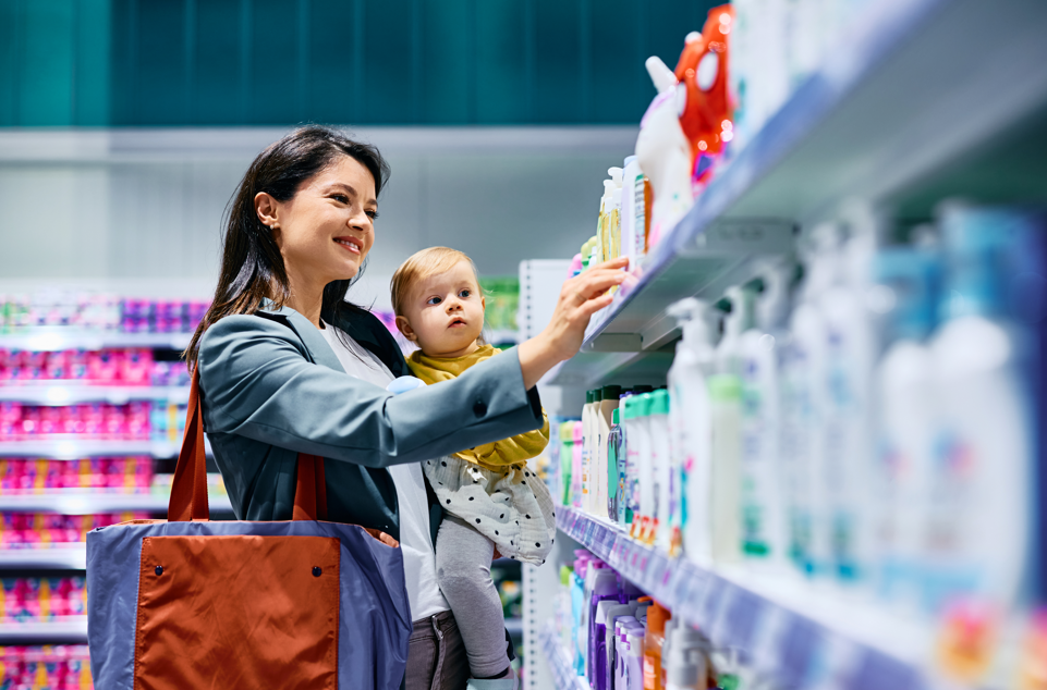 Mother holding infant while shopping for OTC items at a pharmacy