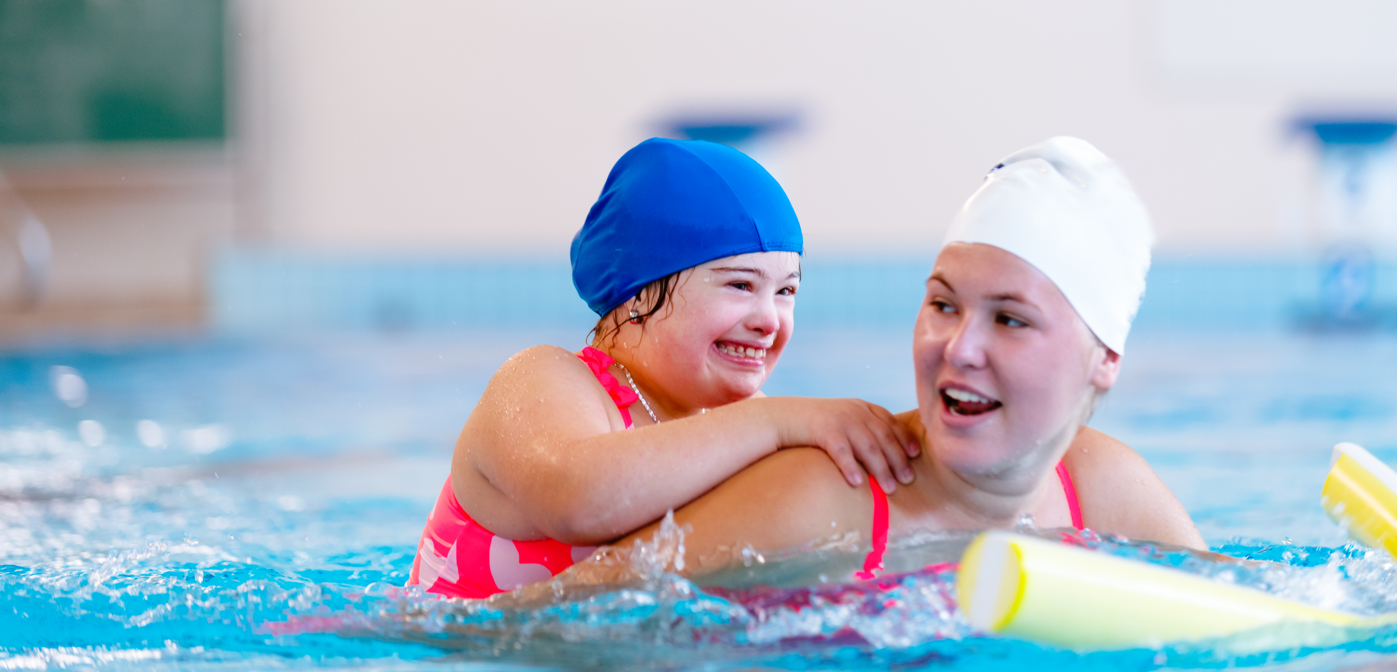Young girl with Down Syndrome swimming with aide.