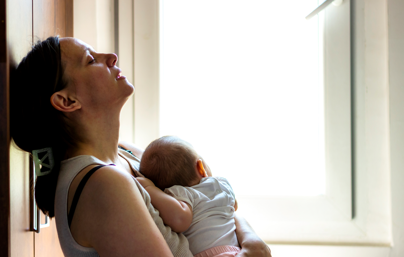 Tired mother holding sleeping newborn